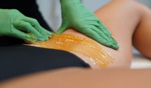 A professional aesthetician performing sugaring hair removal on a client's sensitive skin area using organic sugar paste.