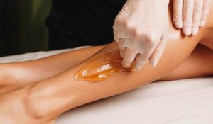 A professional technician applying warm organic paste for sugaring hair removal on a client's leg.